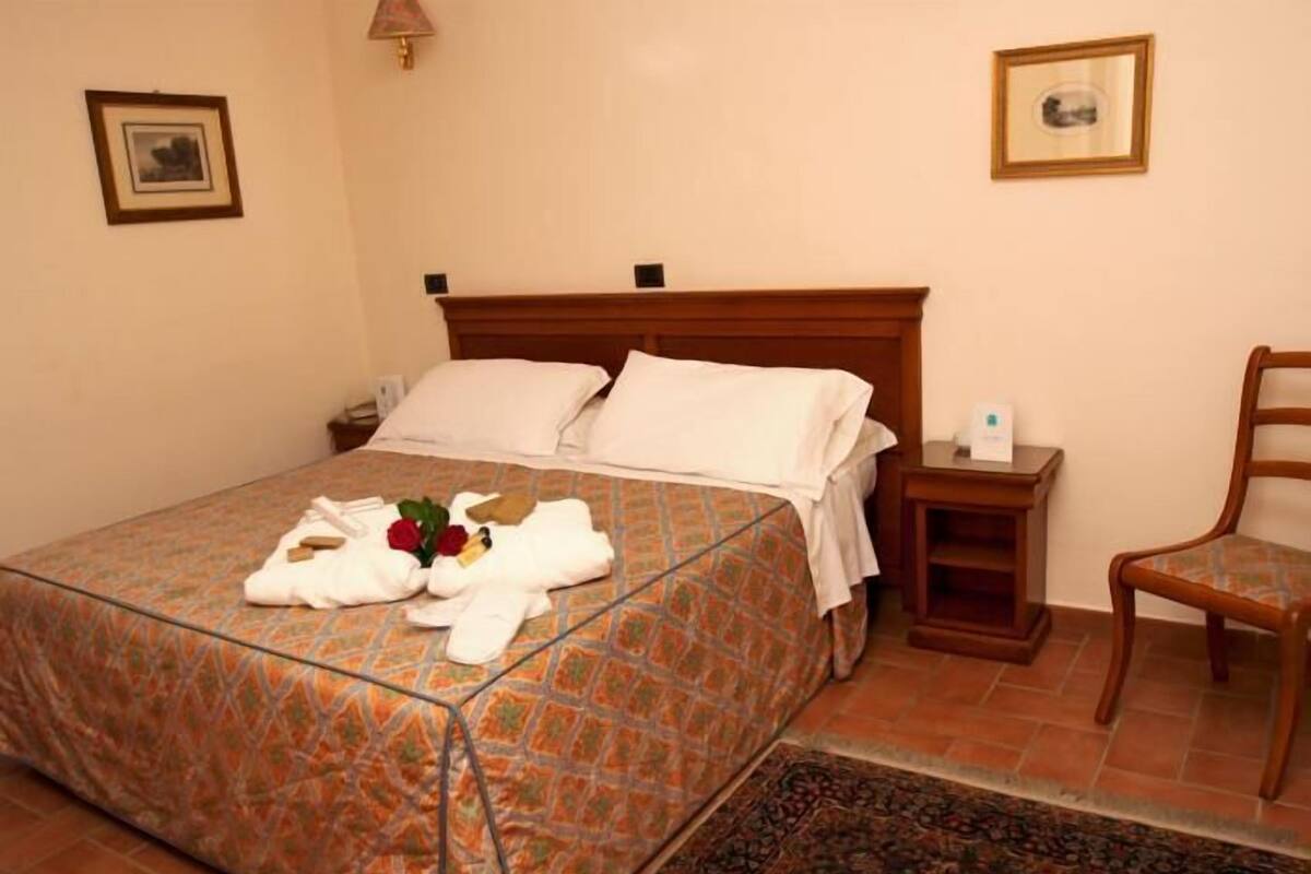 A neatly made bed with a patterned bedspread, a wooden headboard, a small bedside table with a lamp, and a chair.