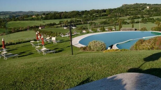 Piscina cercada por grama e espreguiçadeiras, com vista para colinas ondulantes ao fundo.