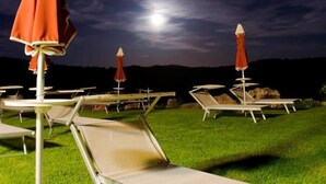 Cadeiras de descanso ao ar livre e guarda-sóis numa área gramada com vista para a lua no céu.
