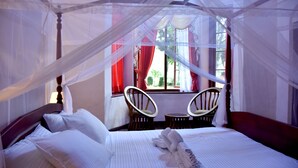 Une chambre à coucher avec un lit à baldaquin, deux fauteuils et une fenêtre ornée de rideaux rouges.