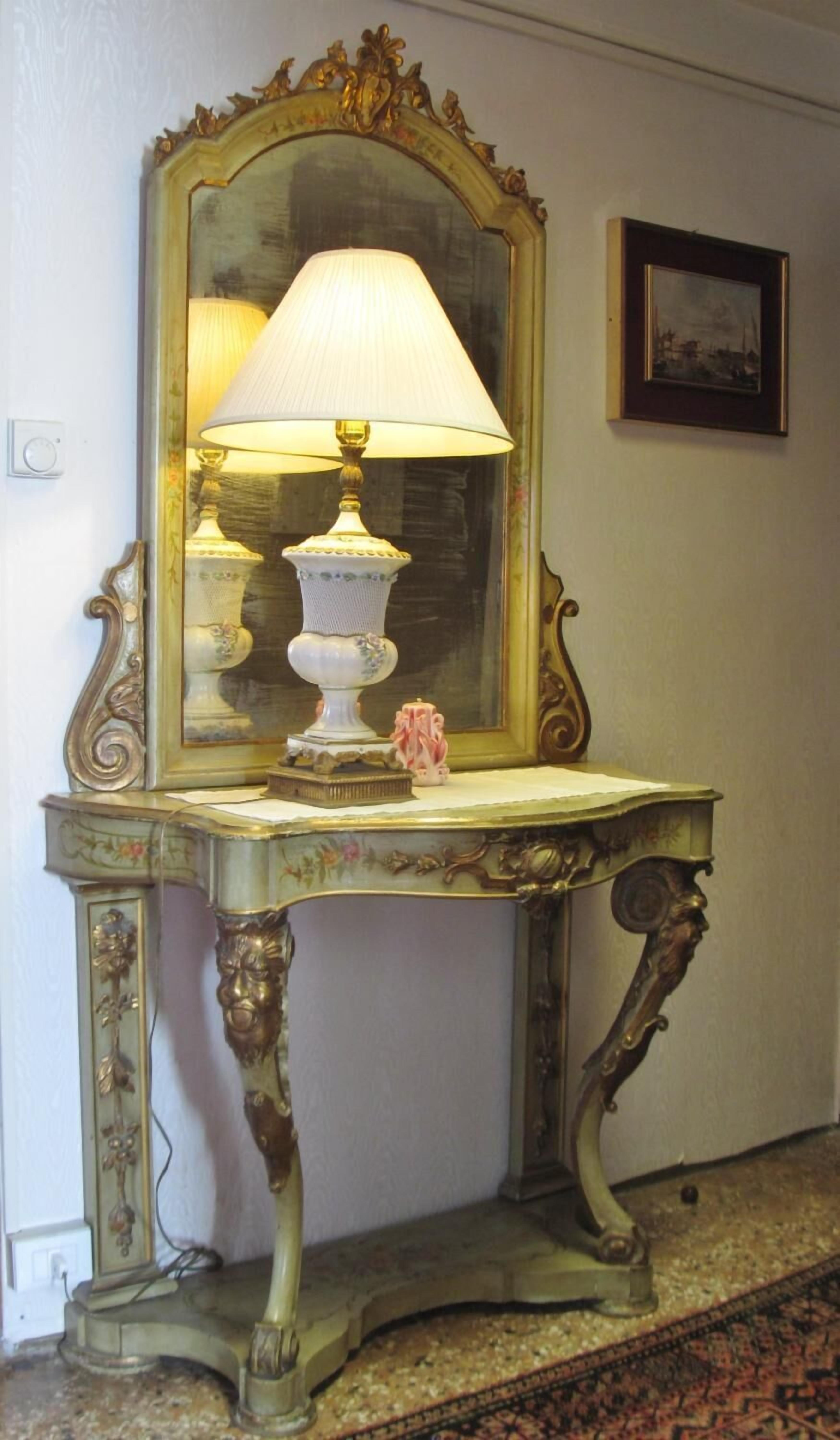 Une console de style vintage, agrémentée d’une lampe, d’un miroir et d’un tableau encadré accroché au mur.