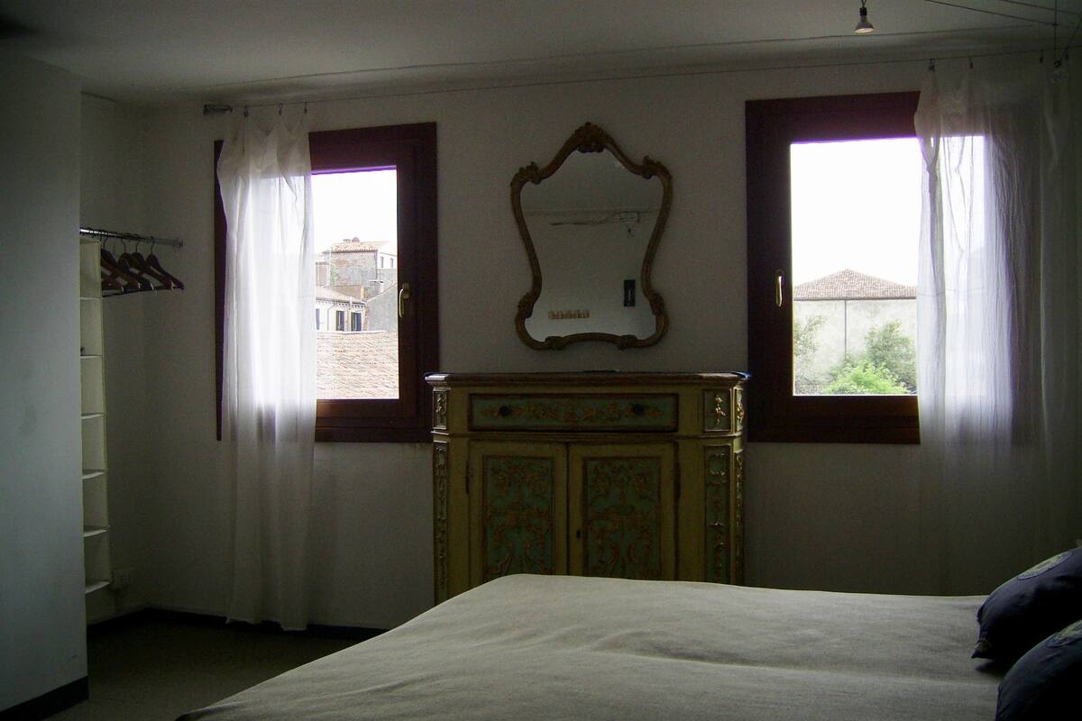A bedroom with a bed, a dresser, and two windows with curtains.