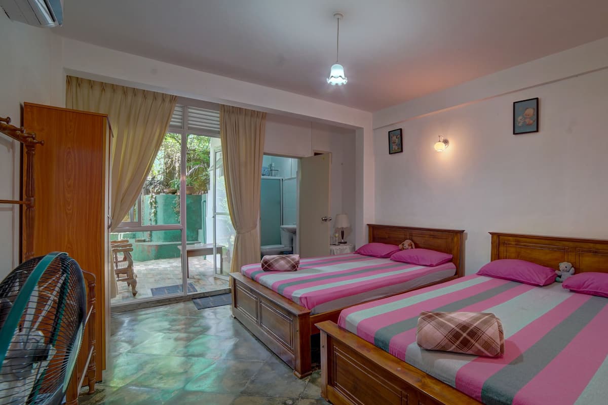 A room with two beds, a wooden wardrobe, a fan, and a window with curtains.