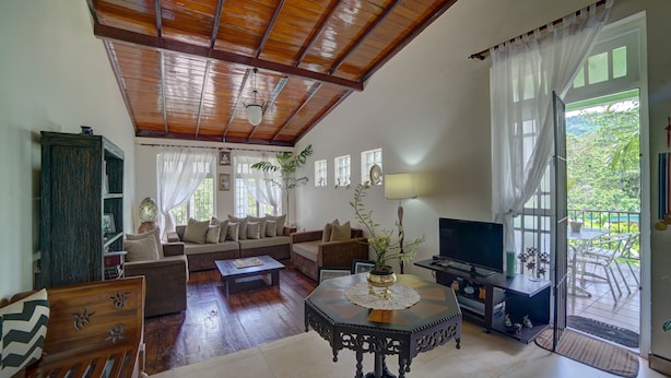 A spacious living room with a wooden ceiling, a sofa set, a coffee table, and a television. - Hanthana Holiday Rooms (Kandy)