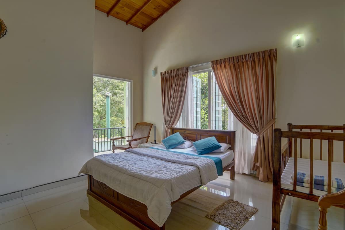 A bedroom with a wooden bed, a chair, a window with curtains, and a view of greenery outside.