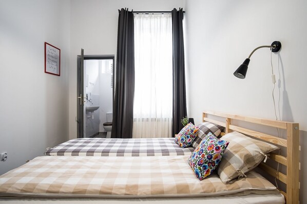 A bedroom with a bed, a bedside lamp, a window with curtains, a sink, and a framed quote on the wall. - HOSTEL likeHome (Przemysl)