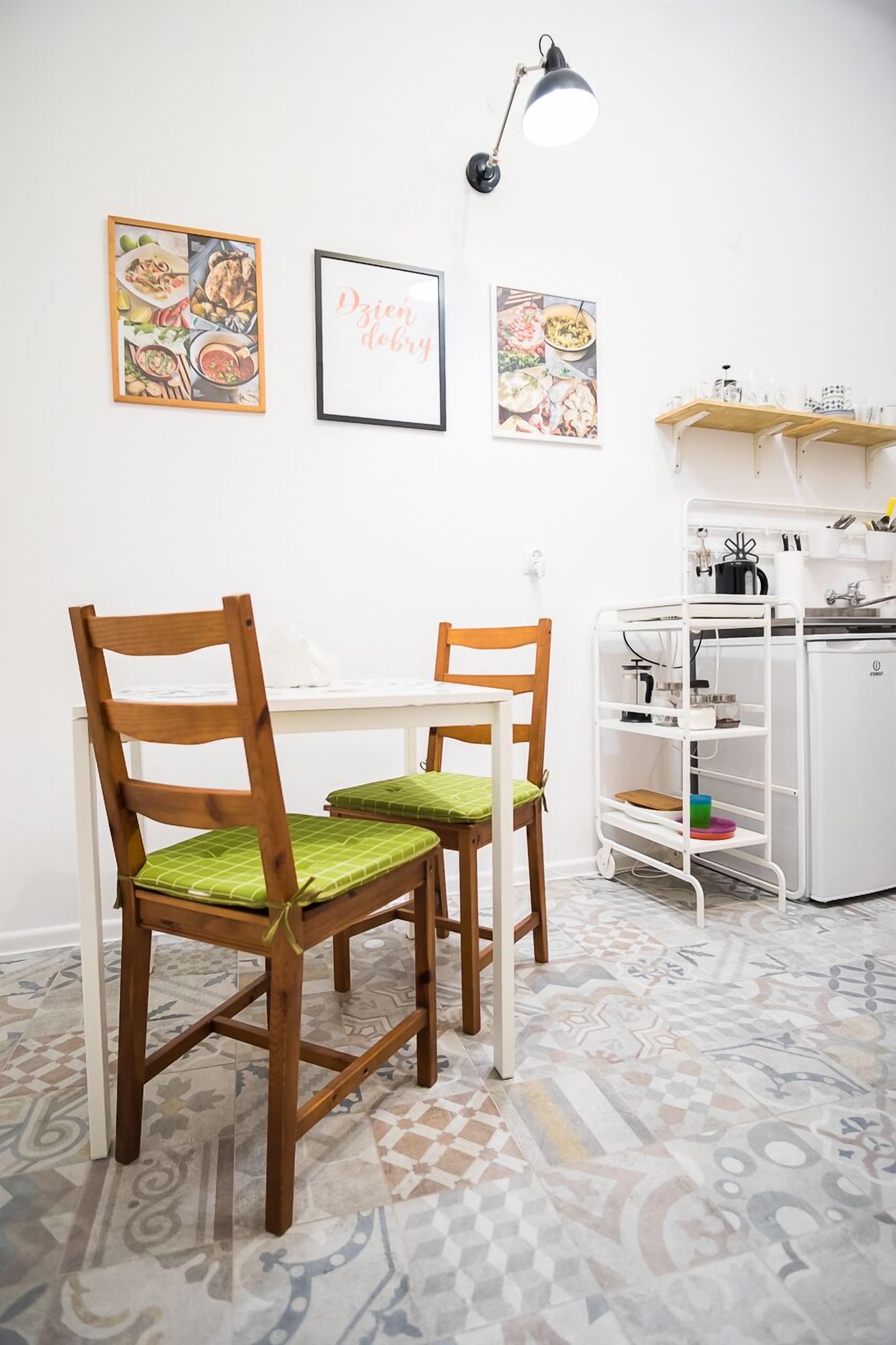 Een eetruimte met twee houten stoelen, een witte tafel en een wit kastje met keukenspullen.