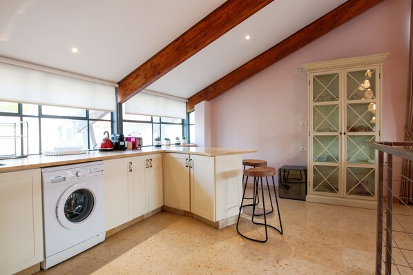 A kitchen with a built-in washer, wooden beams, a bar stool, and a cabinet with glass doors.