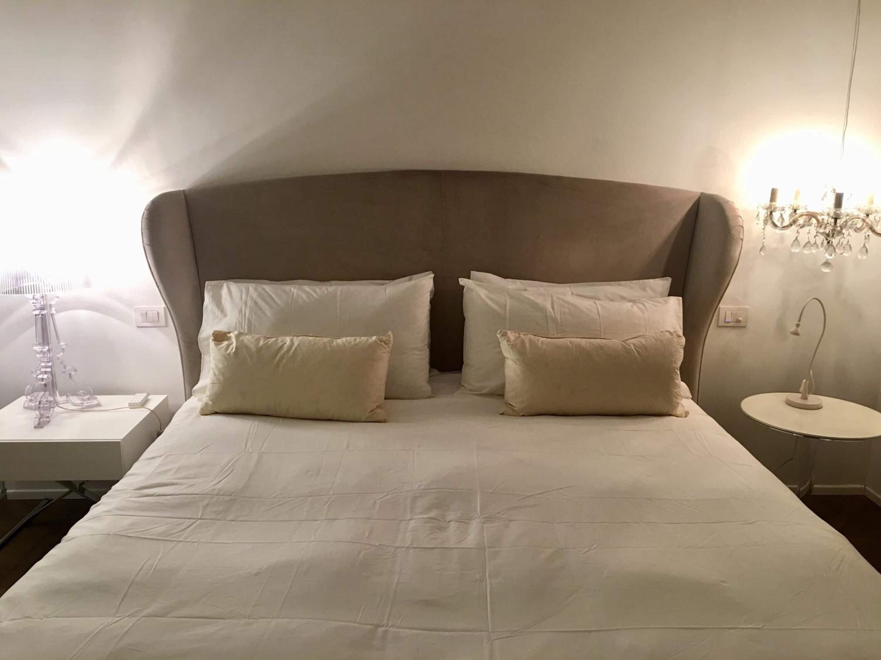 A neatly made bed with a large headboard, two bedside tables, and a chandelier.