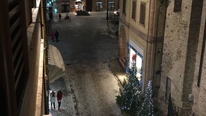 A cobblestone street with buildings on either side, a Christmas tree with lights, and a few people walking. - Luxury My Home (Tolentino)