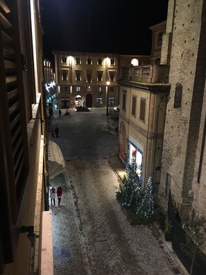 A cobblestone street with buildings on either side, a Christmas tree with lights, and a few people walking. - Luxury My Home (Tolentino)