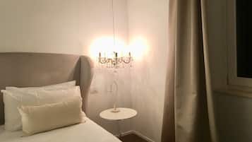 A neatly made bed with white linens and pillows, a small round table with a lamp, and a chandelier with multiple lights.