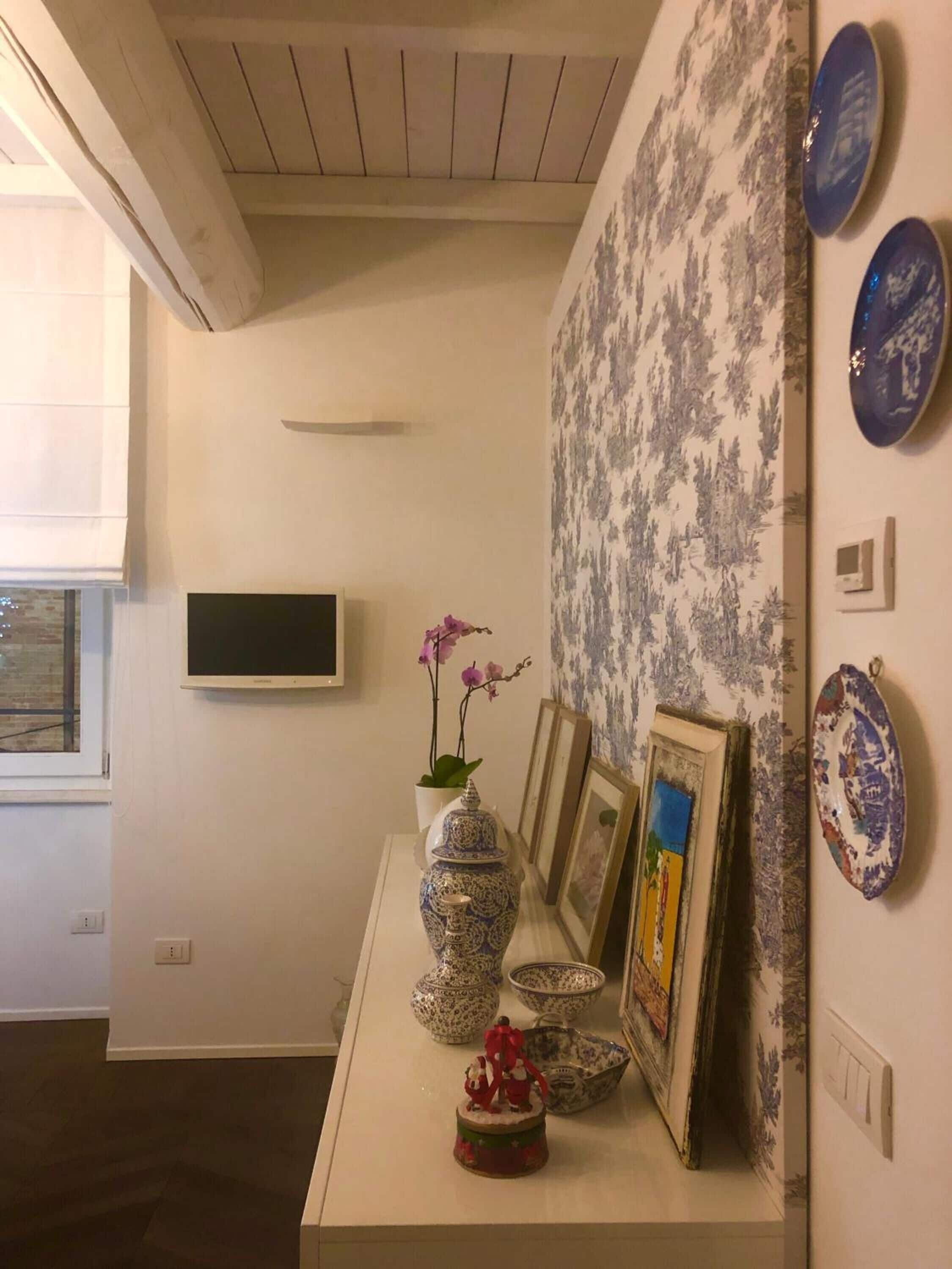 Une pièce avec une table blanche où sont exposés des objets décoratifs, une fenêtre avec des stores et un papier peint à motifs.