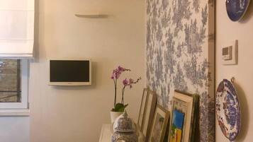 Une pièce avec une table blanche où sont exposés des objets décoratifs, une fenêtre avec des stores et un papier peint à motifs.