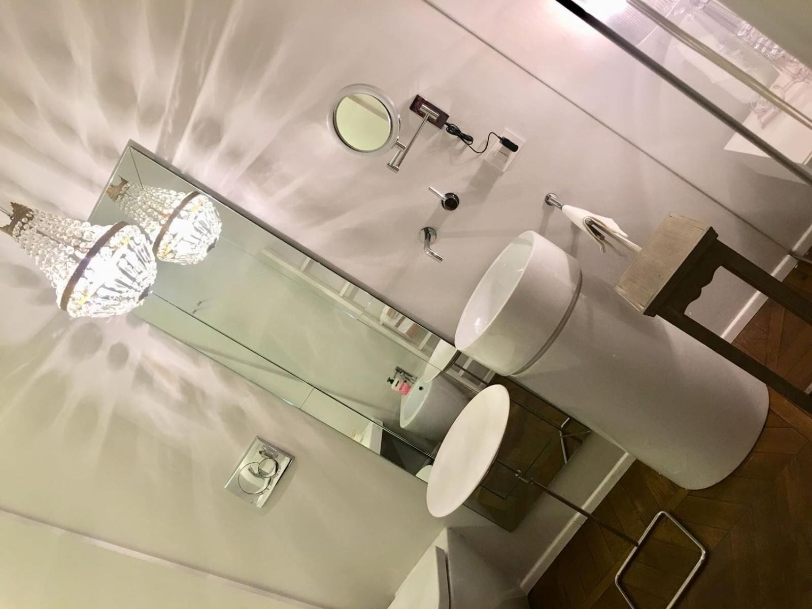 A modern bathroom with a large mirror, a round mirror, a toilet, and a sink.