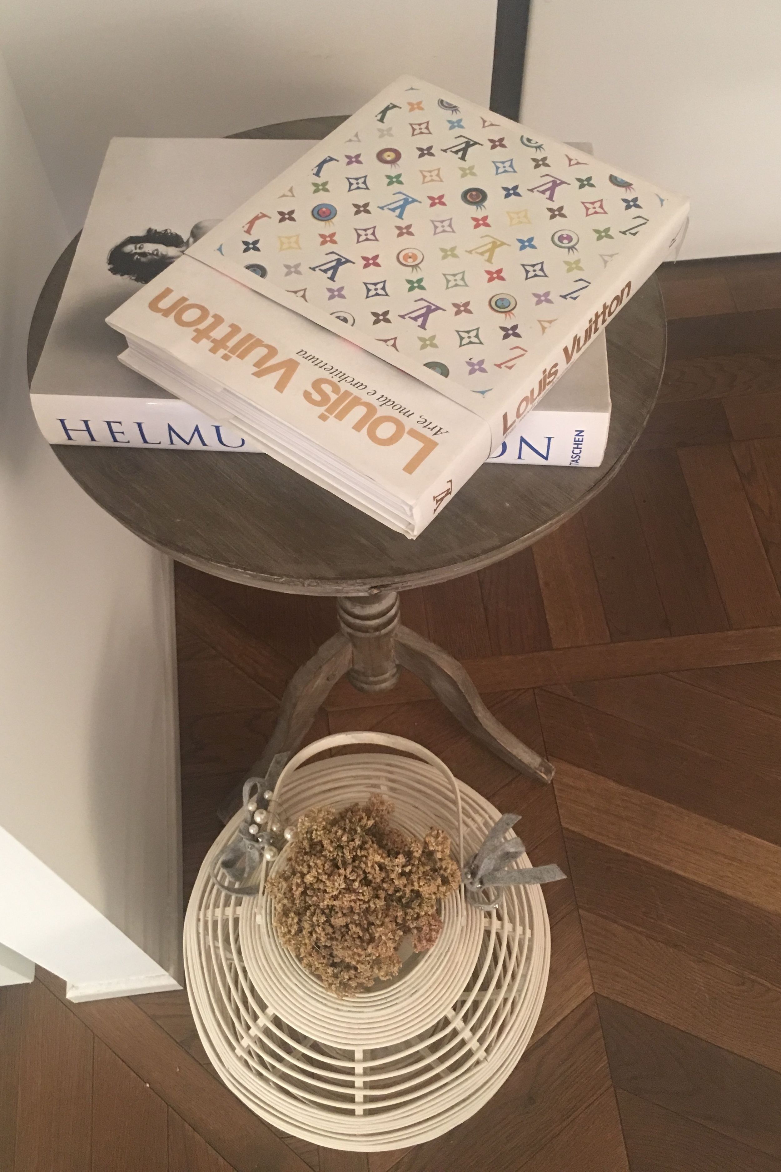 Una mesa con una pila de libros, una cesta con un objeto metálico y un suelo de madera.