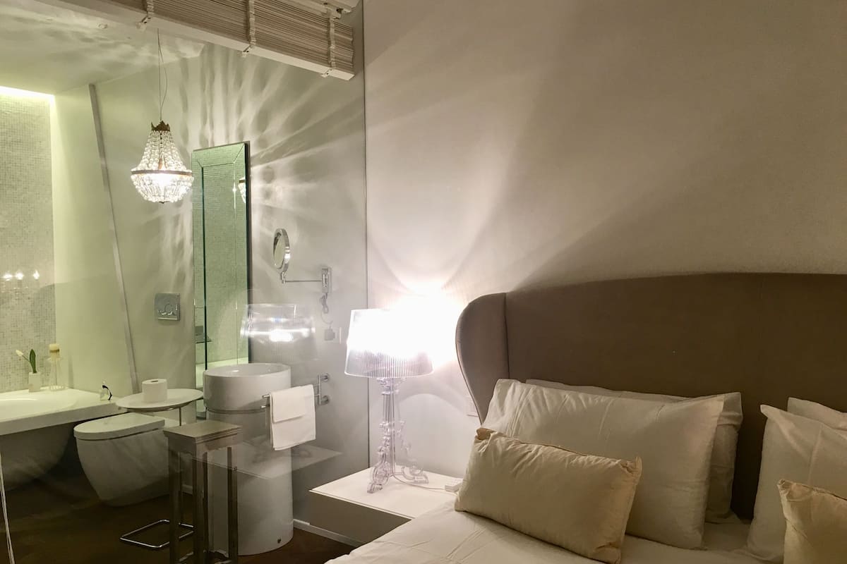 Ein Hotelzimmer mit einem großen Bett, einem Nachttisch, einem Spiegel, einem Waschbecken und einer Toilette.