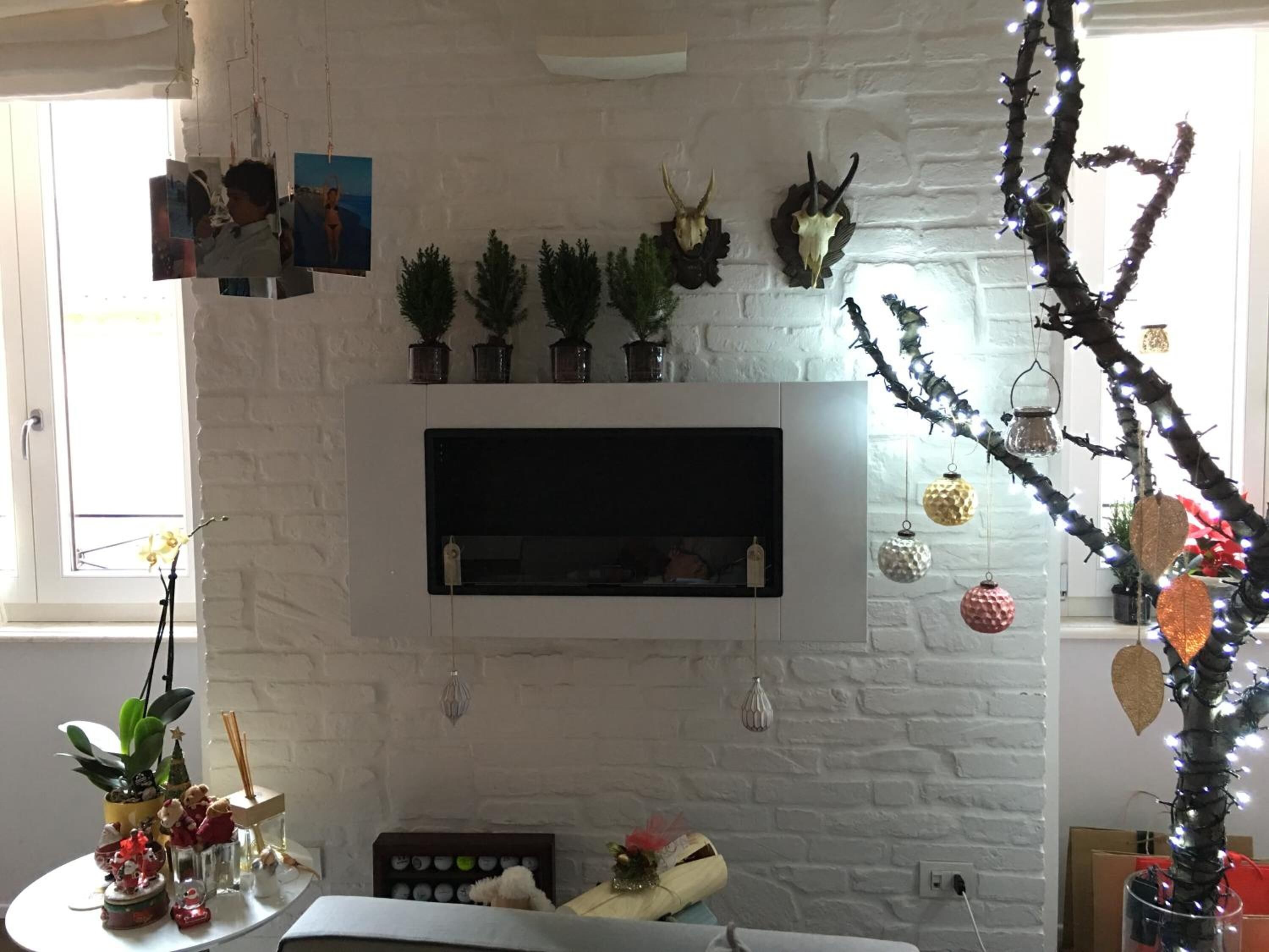 A living room with a white brick wall, a mounted flat-screen TV, and a Christmas tree with lights.