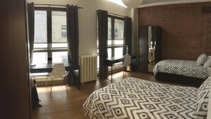 A bedroom with a bed, a desk, a chair, a radiator, and a brick wall. - Granville Hall Residence (Halifax)
