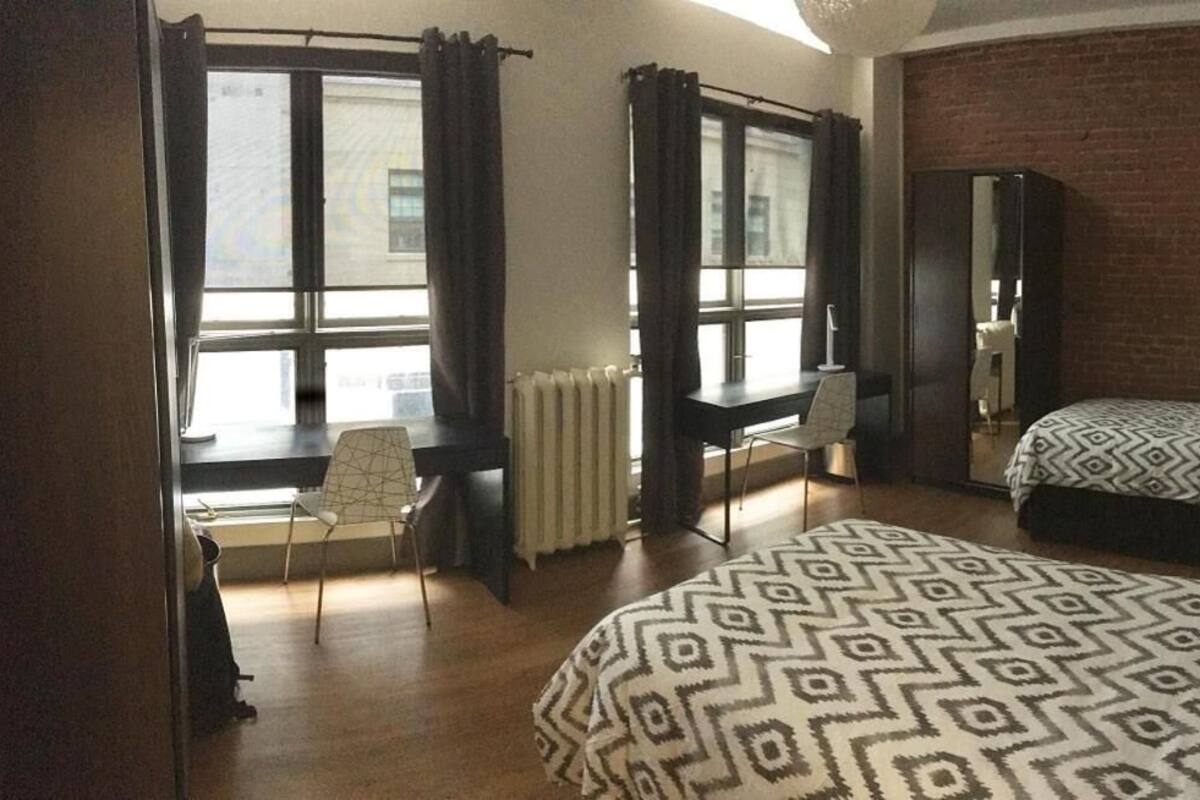 A bedroom with a bed, a desk, a chair, a radiator, and a brick wall.