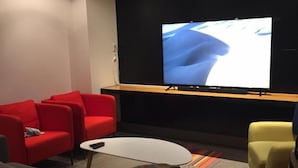 A modern lounge area with a large flat-screen TV, red and yellow seating, and a small coffee table. - Granville Hall Residence (Halifax)