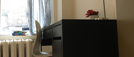 Une pièce comprenant un bureau, une chaise, un radiateur, une fenêtre avec des rideaux et une lampe.