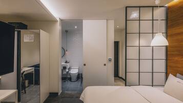 Una habitación de hotel moderna con una cama, un escritorio y un baño visible a través de una puerta abierta.
