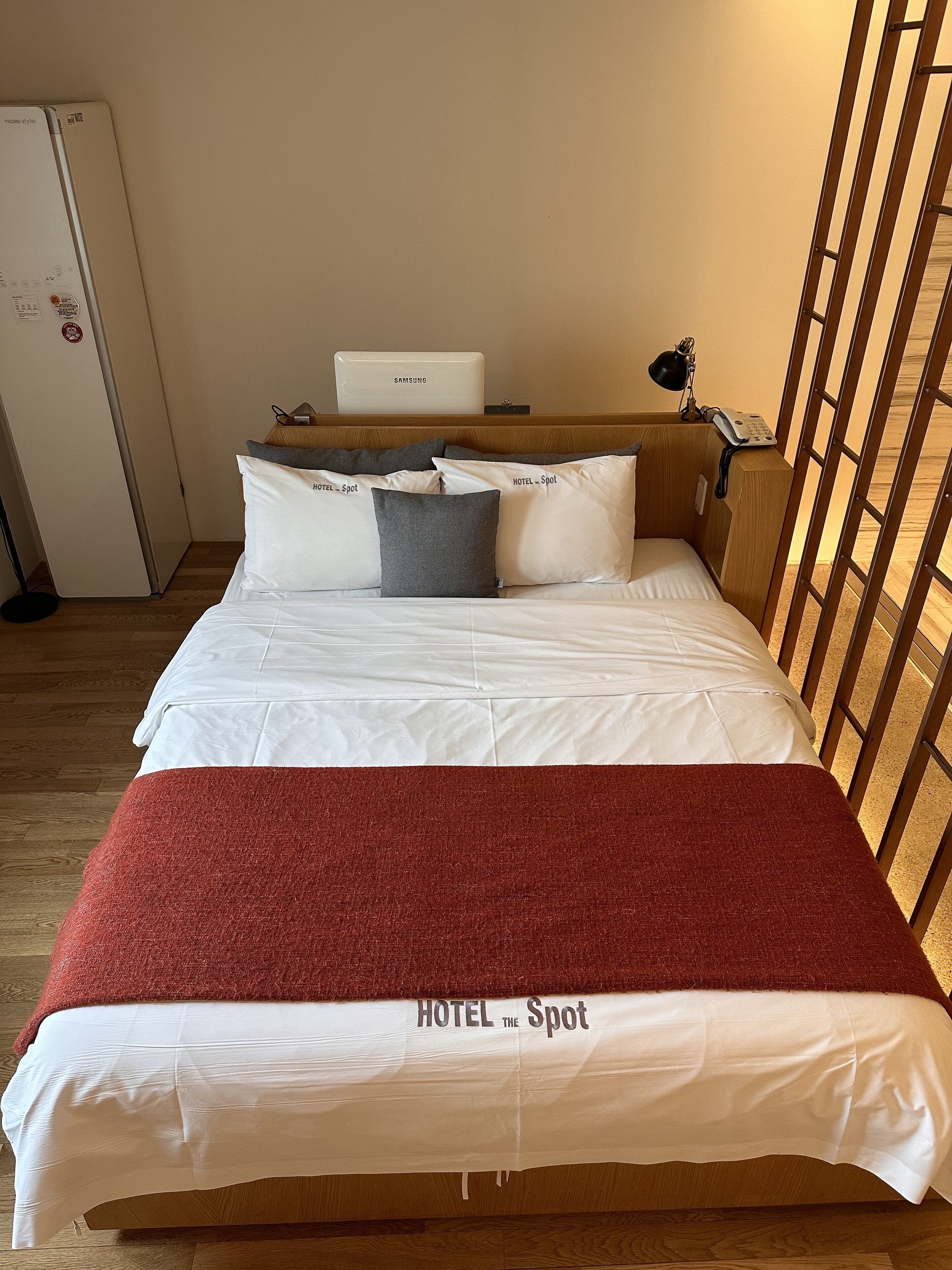 A neatly made bed with white and red bedding, a laptop on a bedside table, and a telephone.