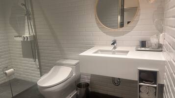 Un baño moderno con un lavabo blanco, un espejo redondo y una cabina de ducha de cristal.