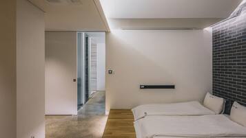 A modern hotel room with a wooden floor, two beds, a brick accent wall, and a minimalist design.