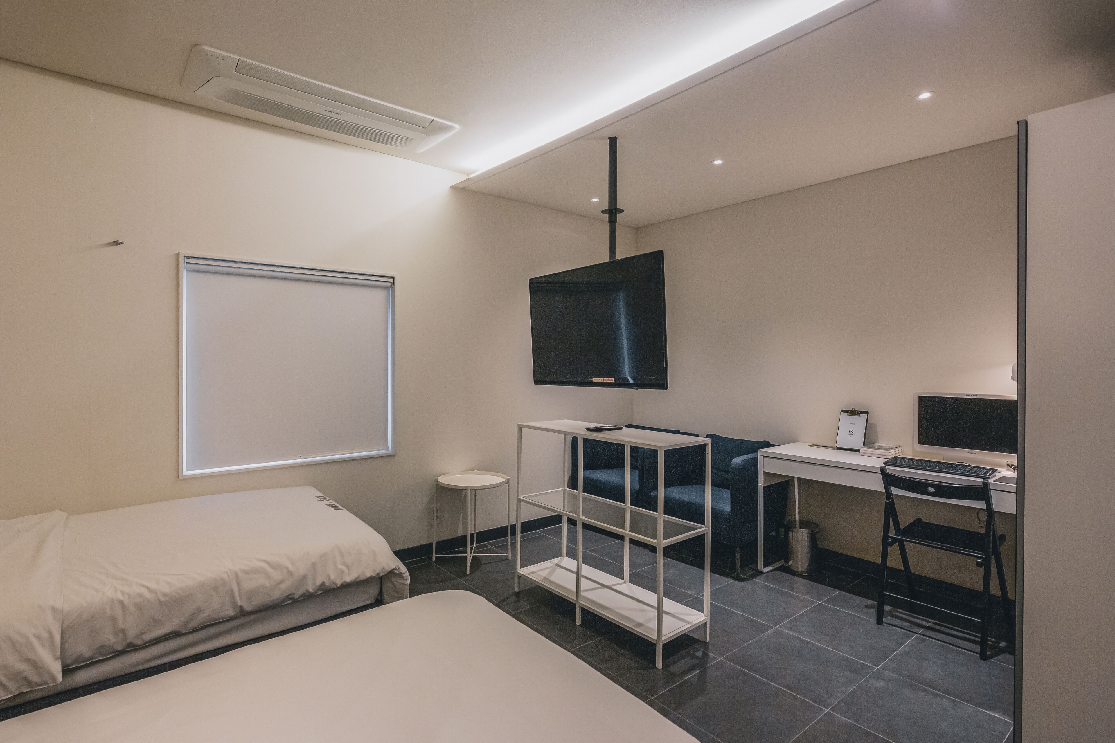Een moderne hotelkamer met een bed, een bureau met een computer, een televisie en een klein bijzettafeltje.