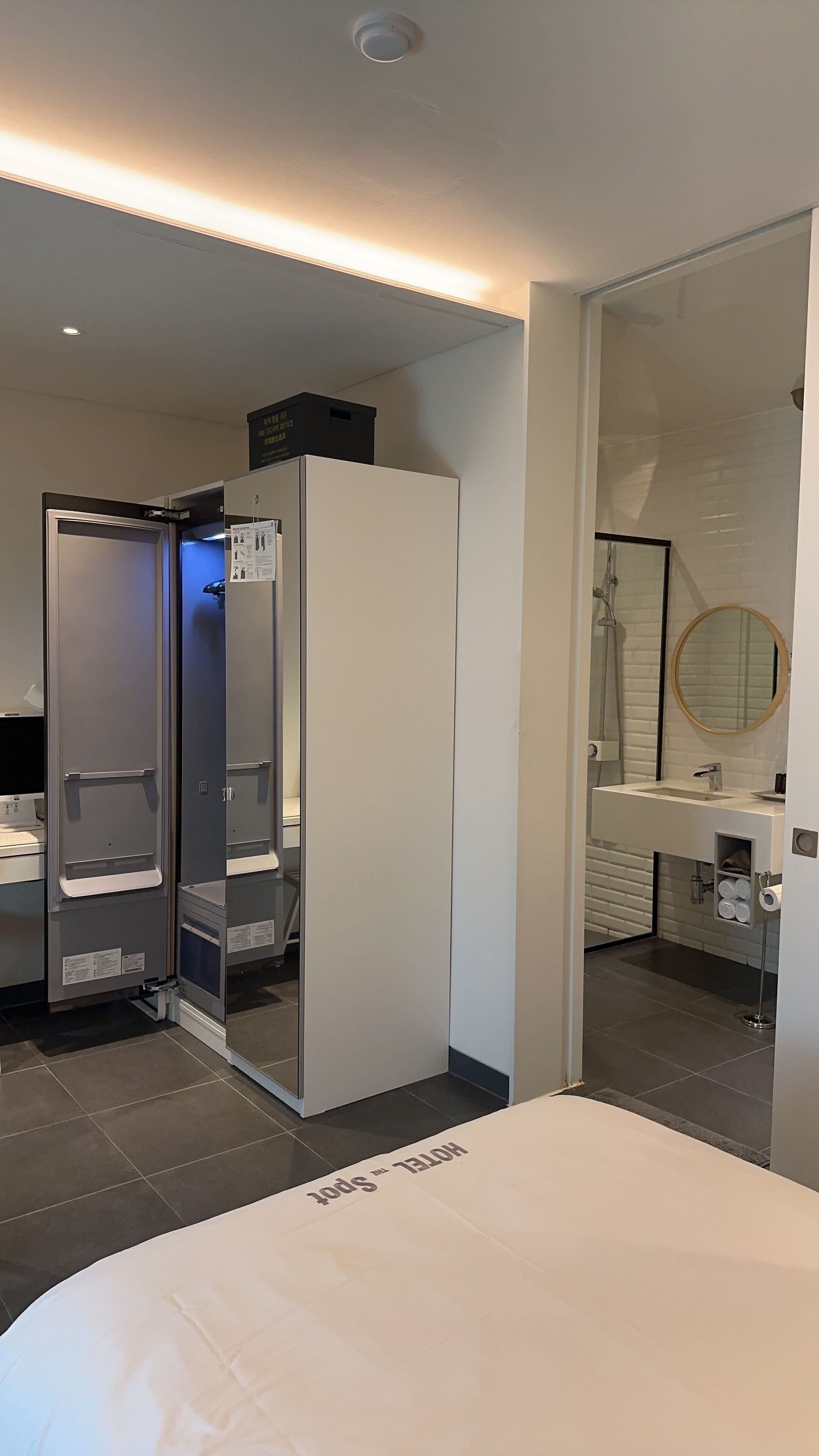 A modern hotel room with a bed, a walk-in closet, a bathroom with a sink and mirror, and a shower.