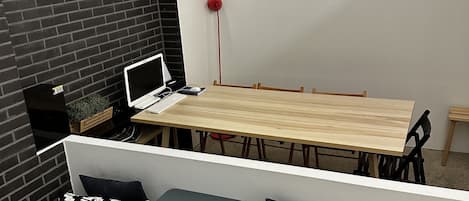 A modern dining area with a wooden table, black and white patterned cushions, and a laptop on a small table.