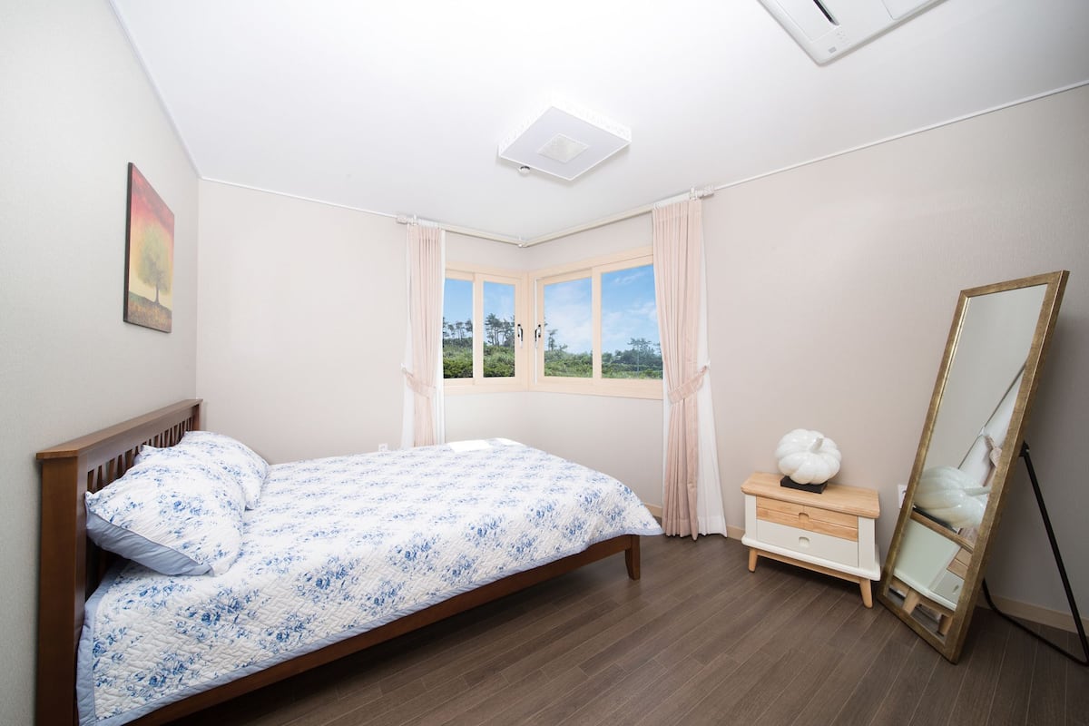 Une chambre à coucher avec un lit en bois, une table de chevet, un miroir et une fenêtre avec des rideaux.