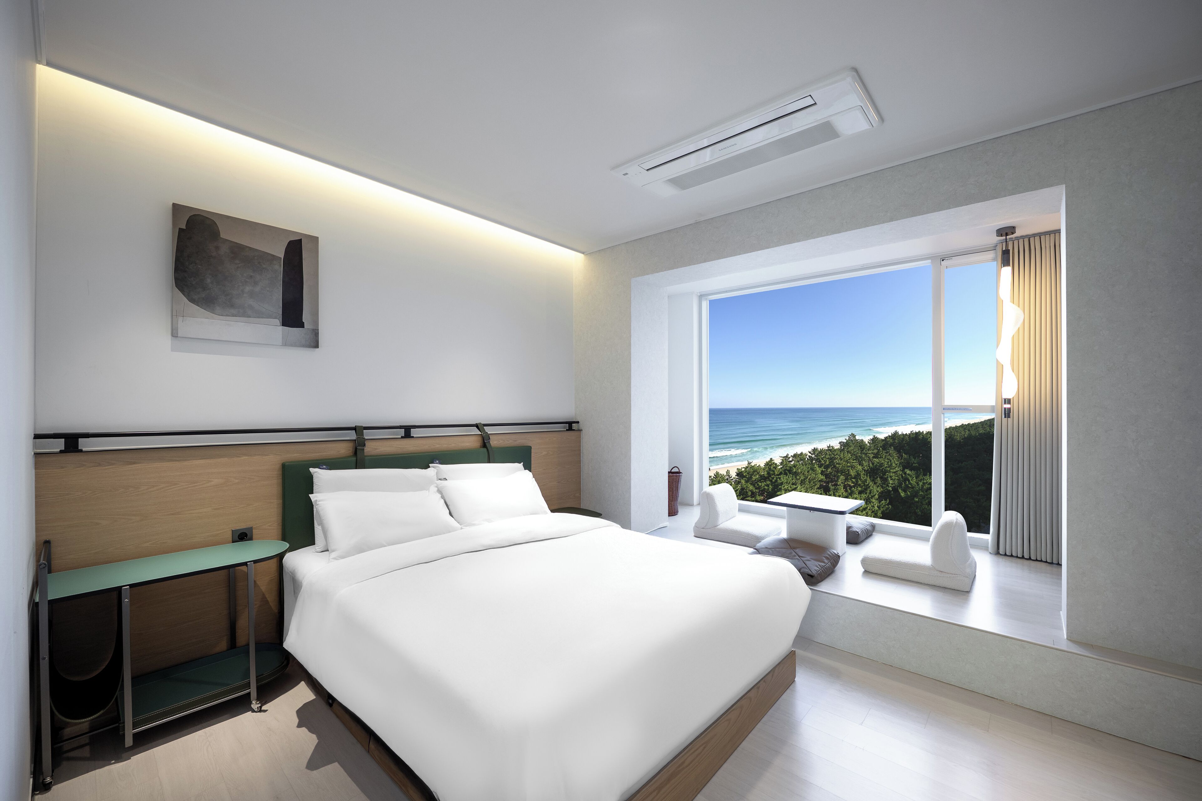 A modern bedroom with a large bed, a desk, and a view of the ocean.