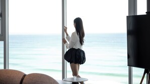 A room with a large window overlooking the ocean, a round table with a glass, and a blackboard. - Hound The Blue (Gangneung)