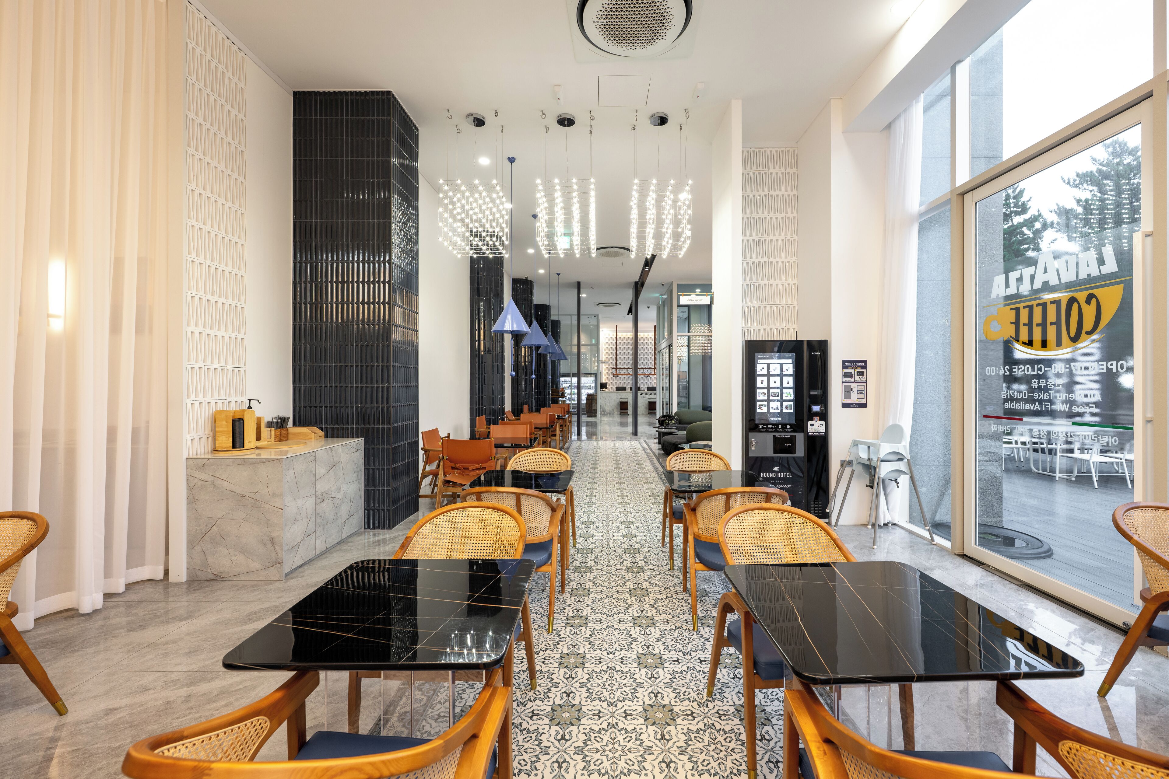 A modern cafe with black tables and wicker chairs, a patterned floor, and a view through the glass wall.