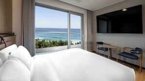 A hotel room with a large bed, a desk with chairs, a TV, and a view of the ocean. - Hound The Blue (Gangneung)