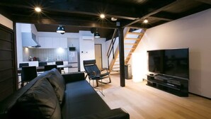 A modern living room with a black leather sofa, a flat-screen TV, and a dining area with a kitchen in the background. - Kyo Koyado Kinkakuji Benten (Kyoto)