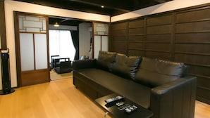 A modern living room with a dark leather sofa, a black coffee table with remotes, and a traditional Japanese sliding door. - Kyo Koyado Kinkakuji Benten (Kyoto)