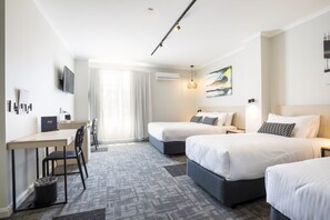 Hotellihuoneessa on kaksi sänkyä, työpöytä ja tuoli. Seinälle on asennettu televisio, sängyn yläpuolella on taulu ja ikkunassa on verhot.