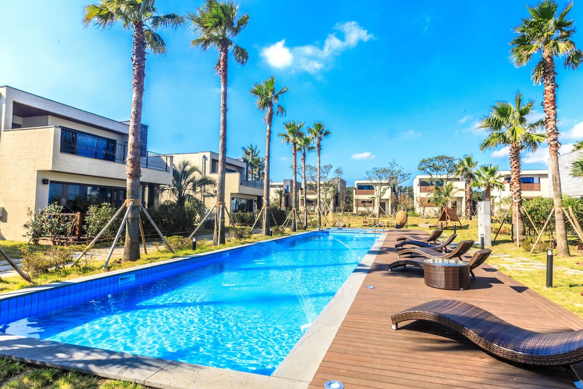 A swimming pool with lounge chairs and palm trees, surrounded by modern buildings.