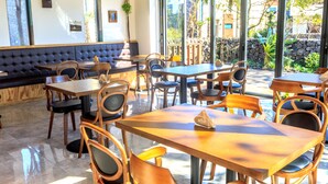 A restaurant with wooden tables and chairs, a cushioned bench, and large windows offering a view of the outdoors. - Marvillrick Spa&Poolvilla (Jeju City)