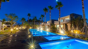 A swimming pool with a wooden deck, surrounded by palm trees and modern buildings.