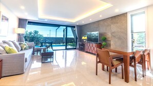 A modern living room with a glass door leading to a pool, a dining area with wooden furniture, and a flat-screen TV on a marble wall. - Marvillrick Spa&Poolvilla (Jeju City)