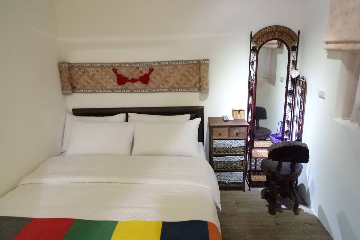 A bedroom with a bed, a nightstand, a mirror, and a chair.