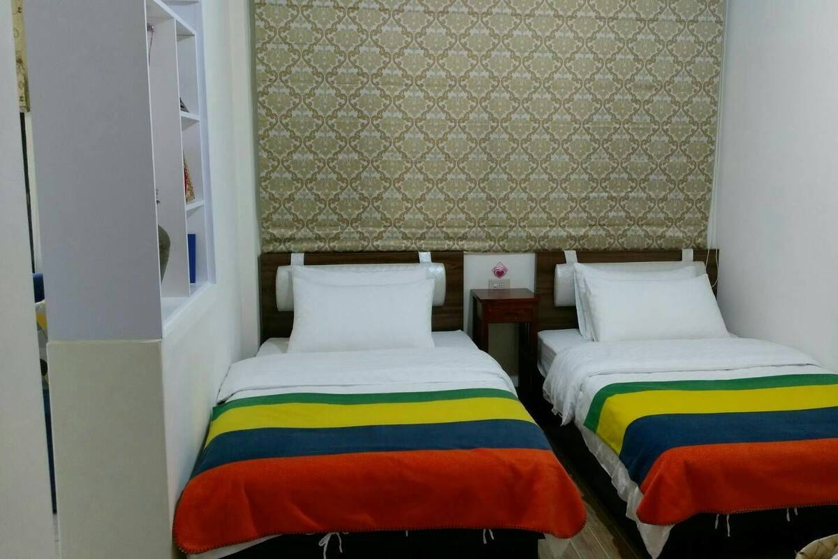 A small, clean room with two single beds, a wooden headboard, and a patterned wall.
