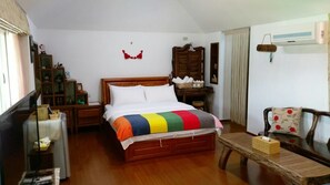Ein Schlafzimmer mit einem hölzernen Bett, einem Nachttisch, einem Sessel, einem kleinen Tisch mit Taschentuchbox und einem Fenster mit Vorhängen.