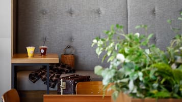 A seating area with a grey upholstered bench, a wooden table with two drinks, a wicker basket, and a plaid blanket.