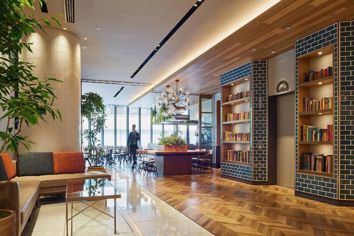 A modern interior with a herringbone wood floor, a central seating area with a glass table, and a brick-patterned bookshelf.